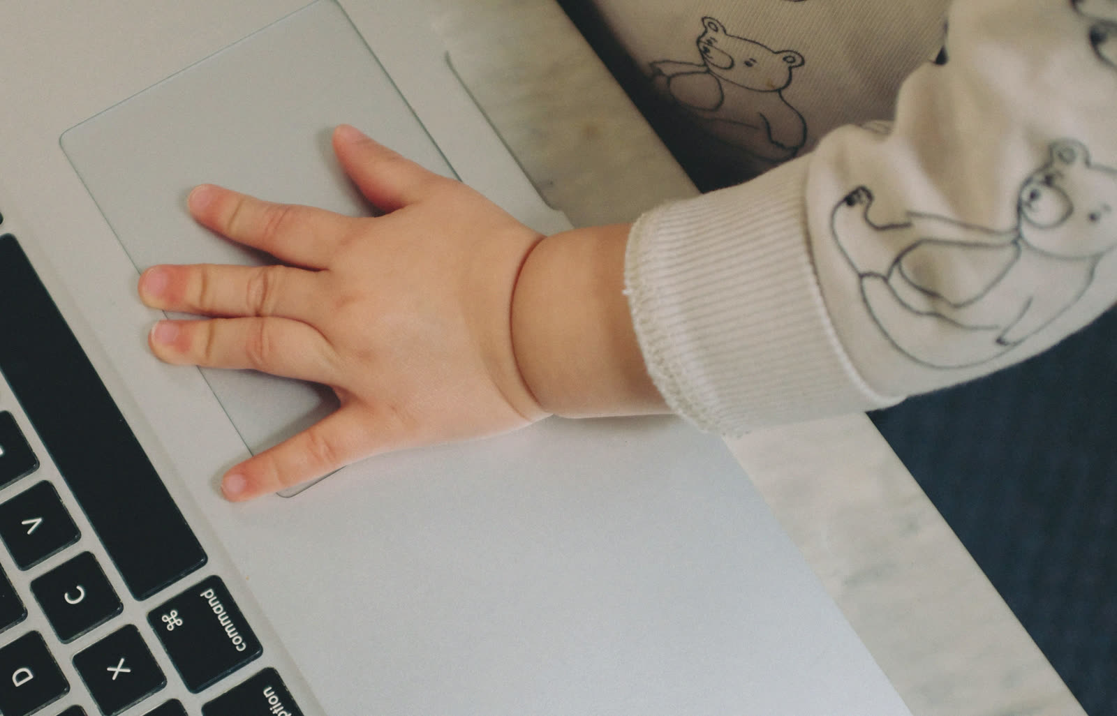 A baby's hand resting on a laptop trackpad.