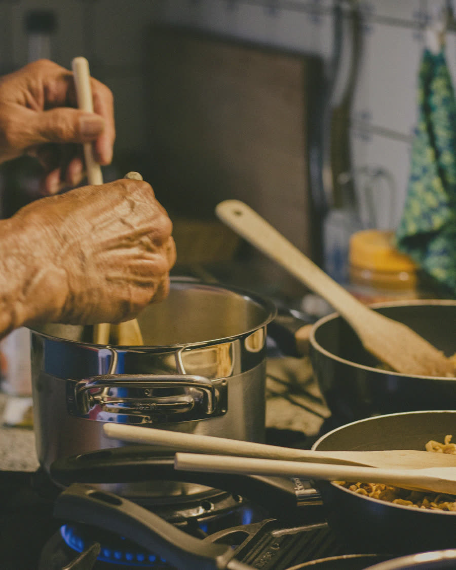 An older person's hands cooking at a stove.